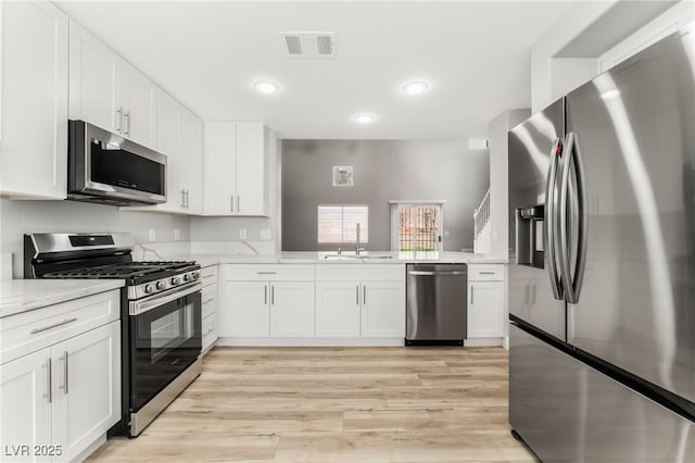 kitchen featuring sink, white cabinetry, light wood-type flooring, stainless steel appliances, and light stone countertops