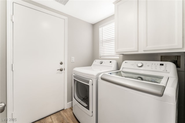 laundry area with washing machine and dryer, cabinets, and light wood-type flooring