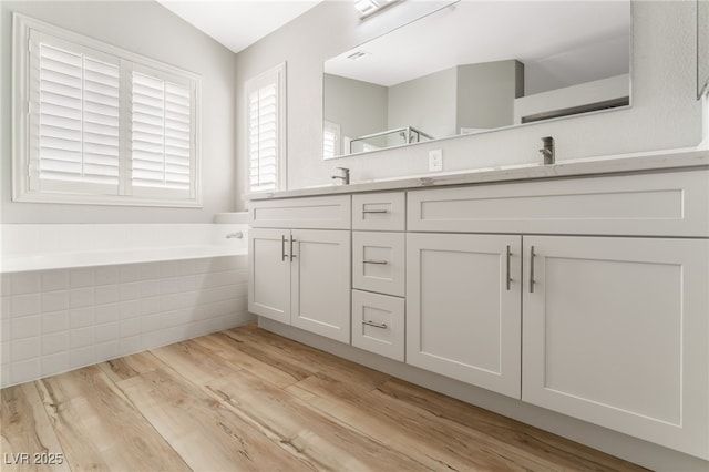 bathroom featuring tiled tub, wood-type flooring, and vanity