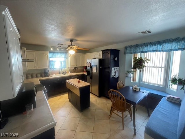 kitchen featuring light tile patterned flooring, a kitchen island, sink, stainless steel fridge with ice dispenser, and a textured ceiling