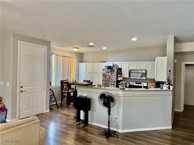 kitchen featuring dark hardwood / wood-style floors, white cabinets, a kitchen breakfast bar, kitchen peninsula, and stainless steel appliances