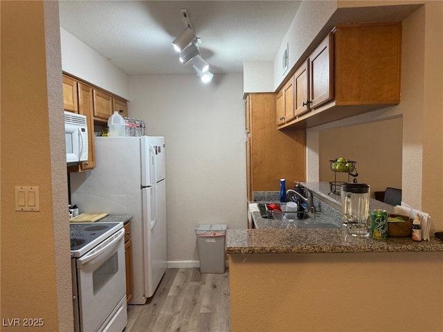 kitchen with sink, light wood-type flooring, track lighting, white appliances, and dark stone counters