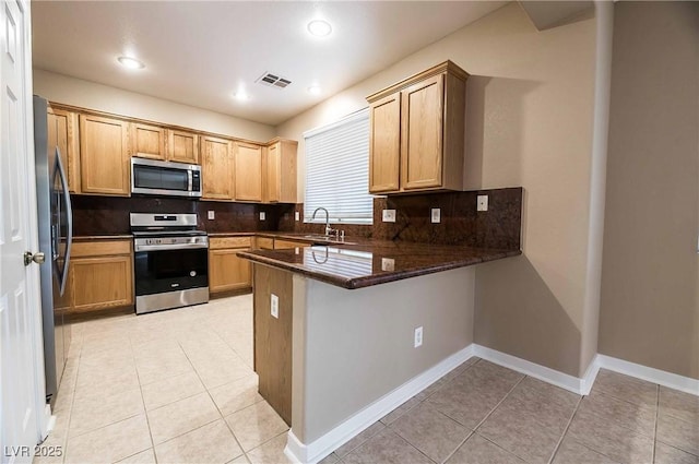 kitchen featuring sink, dark stone countertops, kitchen peninsula, stainless steel appliances, and backsplash