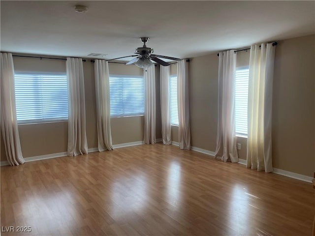 empty room featuring a healthy amount of sunlight, ceiling fan, and light wood-type flooring