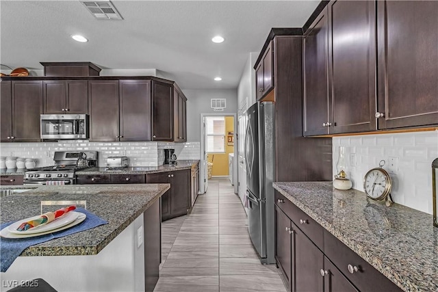 kitchen with tasteful backsplash, appliances with stainless steel finishes, dark brown cabinets, and dark stone countertops