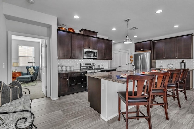 kitchen with a breakfast bar, pendant lighting, an island with sink, dark stone countertops, and stainless steel appliances