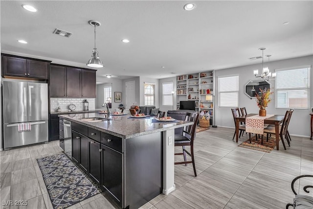 kitchen featuring pendant lighting, sink, stainless steel appliances, light stone countertops, and an island with sink