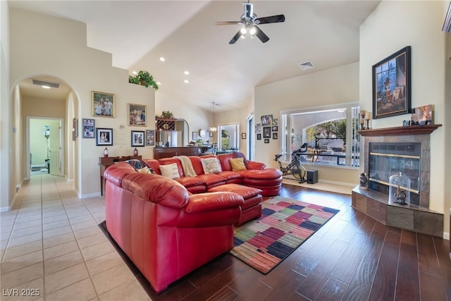 living room with a tile fireplace, light wood-type flooring, ceiling fan, and high vaulted ceiling