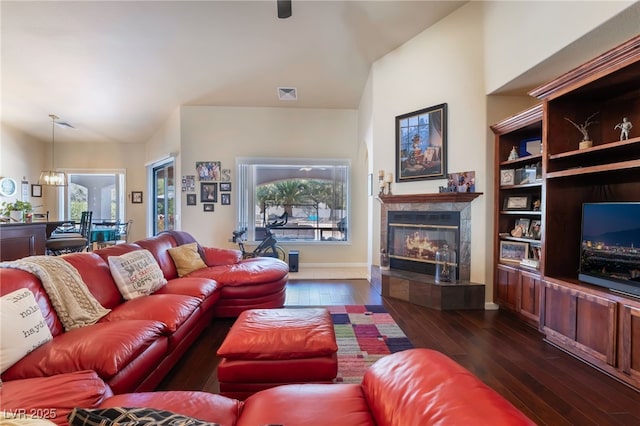 living room featuring an inviting chandelier, dark wood-type flooring, a fireplace, and built in shelves