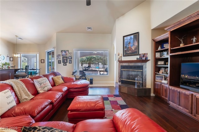 living room with dark hardwood / wood-style flooring, built in features, a tile fireplace, and a chandelier