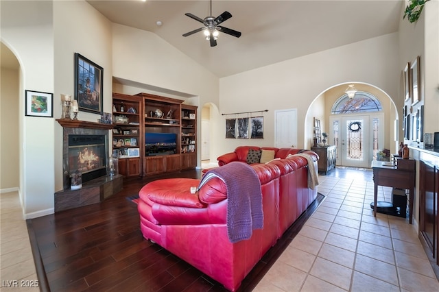 living room featuring a tile fireplace, hardwood / wood-style floors, ceiling fan, and high vaulted ceiling