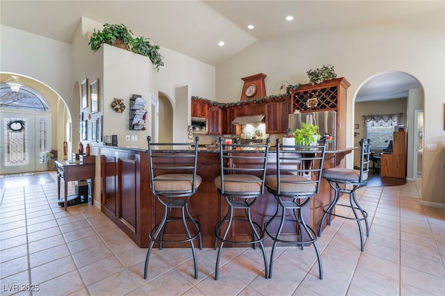 kitchen featuring light tile patterned floors, stainless steel appliances, kitchen peninsula, and high vaulted ceiling