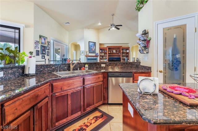 kitchen with light tile patterned flooring, vaulted ceiling, sink, dark stone countertops, and stainless steel dishwasher