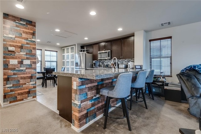 kitchen with a kitchen breakfast bar, light colored carpet, dark brown cabinetry, kitchen peninsula, and stainless steel appliances