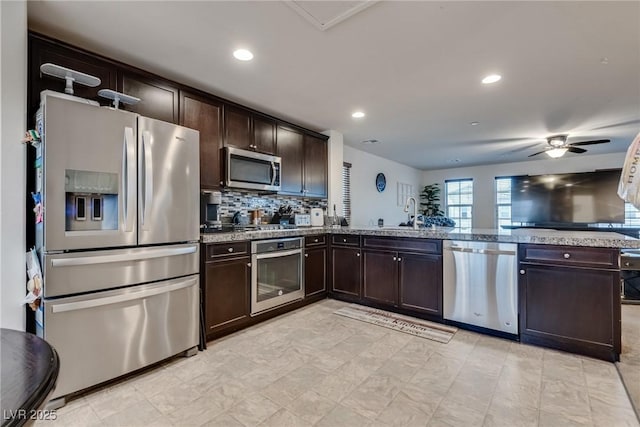 kitchen with stainless steel appliances, light stone countertops, and dark brown cabinetry