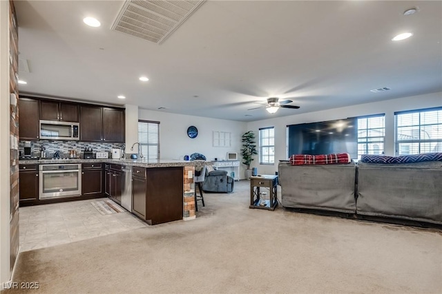 kitchen with appliances with stainless steel finishes, kitchen peninsula, light carpet, and a breakfast bar area