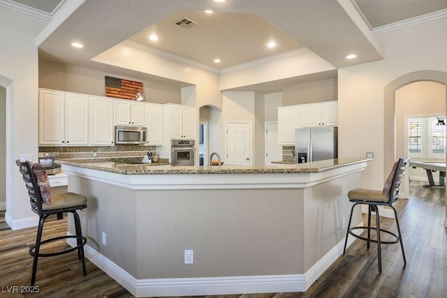 kitchen with arched walkways, appliances with stainless steel finishes, a large island with sink, and white cabinetry