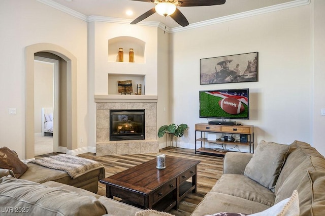 living room with ornamental molding, arched walkways, a tiled fireplace, and wood finished floors