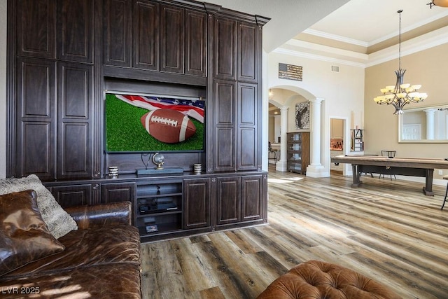 interior space featuring arched walkways, wood finished floors, a raised ceiling, decorative columns, and crown molding