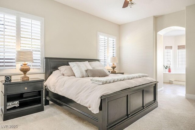 bedroom with ceiling fan, arched walkways, ensuite bathroom, and light colored carpet