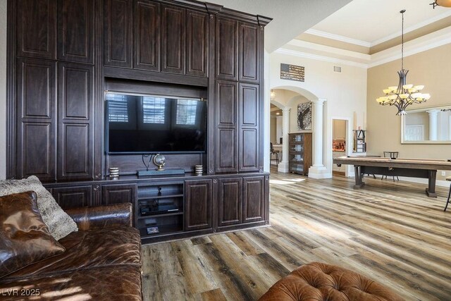 interior space featuring arched walkways, pendant lighting, crown molding, decorative columns, and wood finished floors