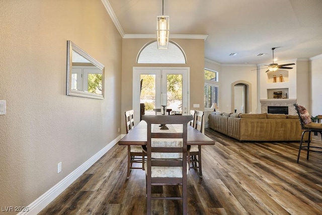 dining room with a fireplace, ornamental molding, dark wood-type flooring, ceiling fan, and baseboards