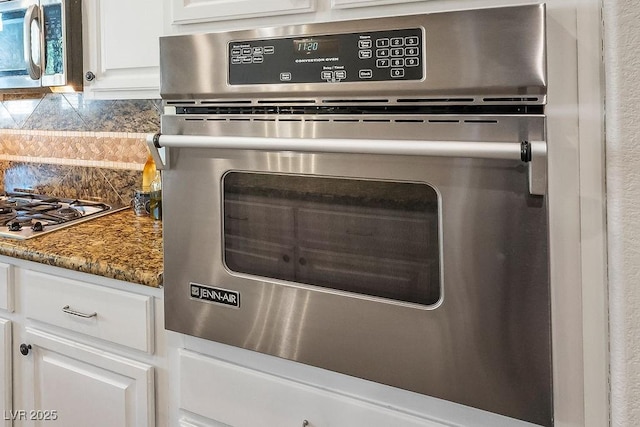 details with stainless steel appliances, dark stone countertops, backsplash, and white cabinetry