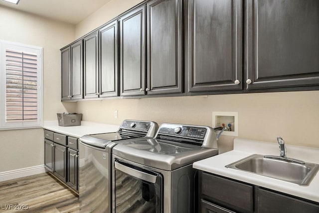 clothes washing area with cabinet space, baseboards, light wood-style floors, separate washer and dryer, and a sink