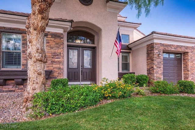 property entrance with a garage, stone siding, a lawn, and stucco siding