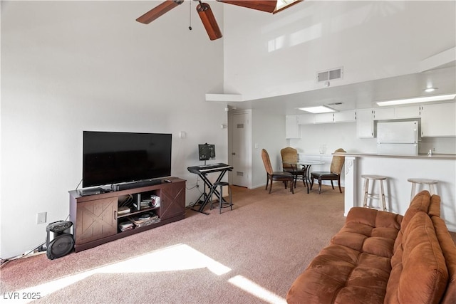 carpeted living room with ceiling fan and a high ceiling