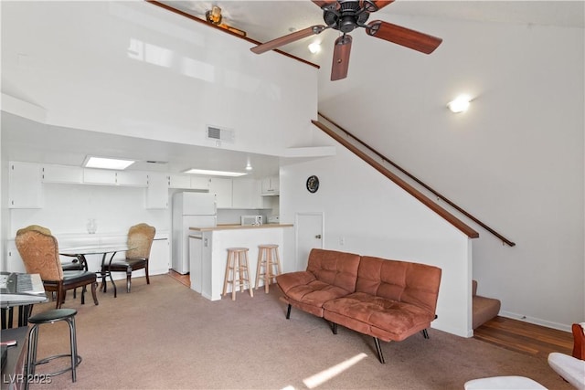 carpeted living room featuring ceiling fan and a towering ceiling