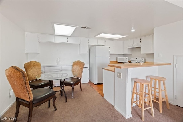 kitchen featuring a kitchen breakfast bar, white cabinetry, white appliances, and kitchen peninsula