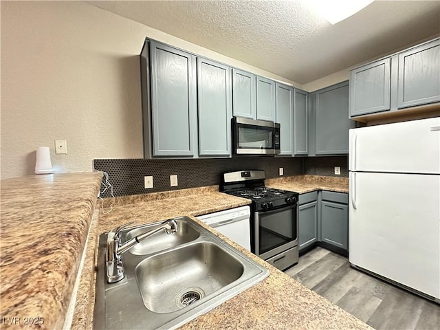 kitchen featuring light wood finished floors, stainless steel appliances, light countertops, a sink, and a textured ceiling