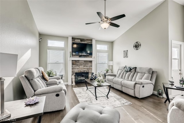 living room with ceiling fan, a stone fireplace, high vaulted ceiling, and light hardwood / wood-style flooring