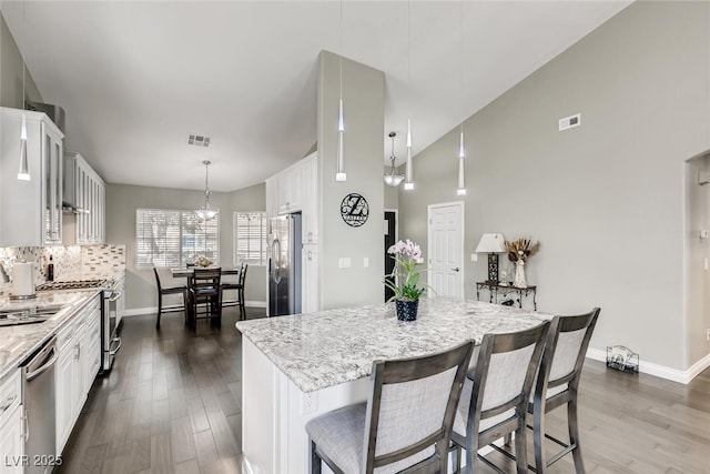 kitchen featuring dark wood-type flooring, a center island, pendant lighting, stainless steel appliances, and white cabinets