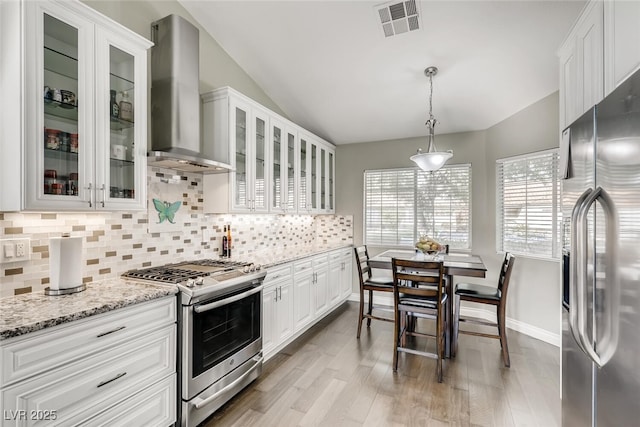 kitchen featuring stainless steel appliances, white cabinetry, pendant lighting, and wall chimney range hood