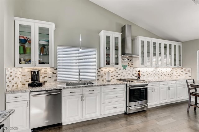 kitchen featuring lofted ceiling, wall chimney range hood, sink, stainless steel appliances, and white cabinets