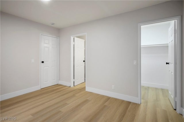 unfurnished bedroom with a spacious closet, a closet, and light wood-type flooring