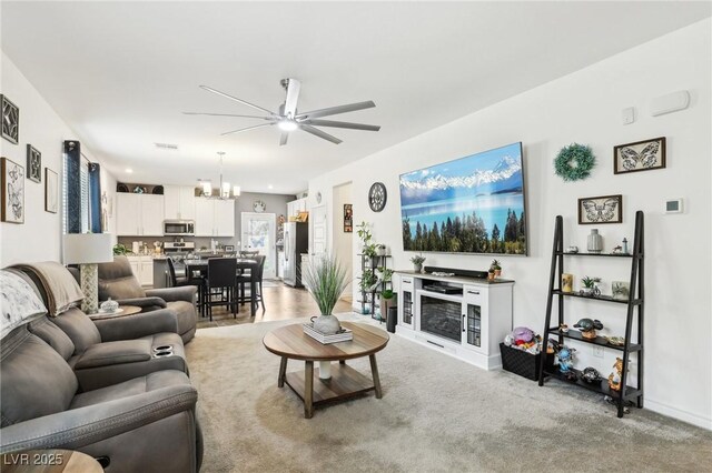 living room featuring ceiling fan with notable chandelier and light carpet