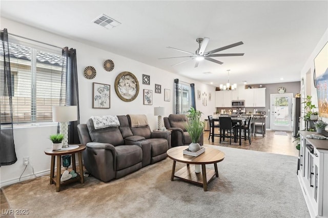 living room with light carpet, baseboards, visible vents, and ceiling fan with notable chandelier