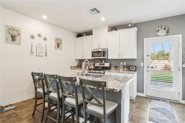 kitchen with visible vents, appliances with stainless steel finishes, a kitchen island with sink, white cabinets, and a kitchen bar