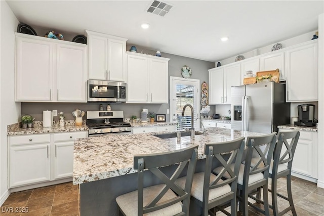 kitchen with appliances with stainless steel finishes, a kitchen island with sink, a sink, and white cabinetry