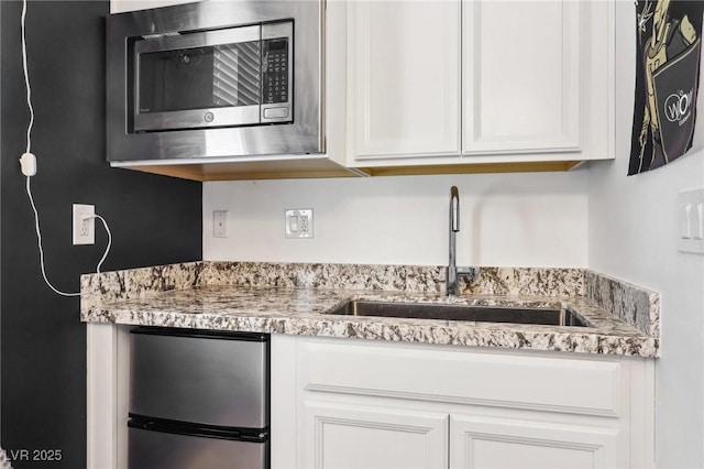 kitchen featuring appliances with stainless steel finishes, white cabinetry, a sink, and light stone counters