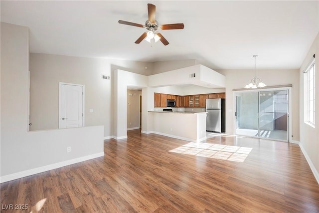 unfurnished living room with lofted ceiling, ceiling fan with notable chandelier, visible vents, baseboards, and light wood-style floors