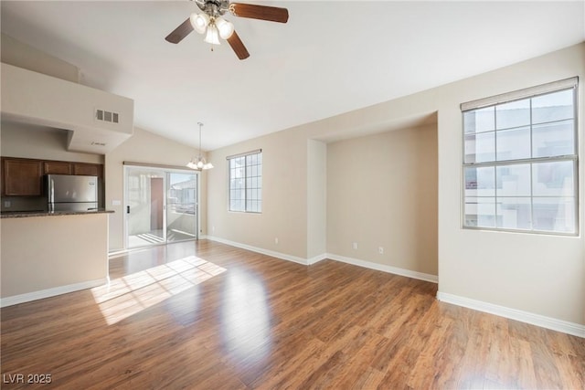 unfurnished living room with vaulted ceiling, ceiling fan with notable chandelier, and light hardwood / wood-style floors