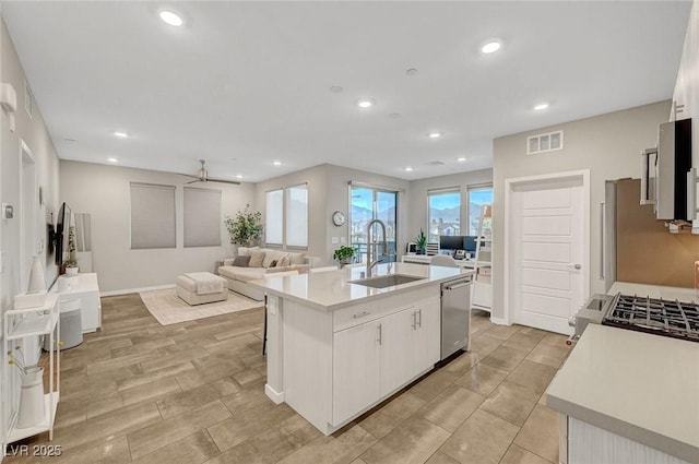 kitchen with sink, white cabinets, a kitchen island with sink, stainless steel dishwasher, and ceiling fan