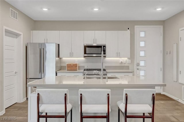 kitchen featuring stainless steel appliances, an island with sink, sink, and white cabinets