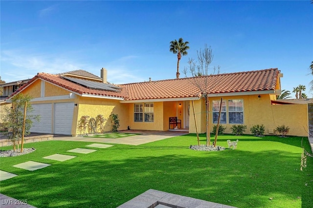 back of property featuring a garage, a yard, and solar panels