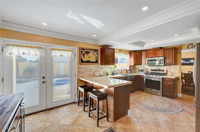 kitchen featuring stainless steel appliances, a kitchen breakfast bar, a tray ceiling, french doors, and kitchen peninsula