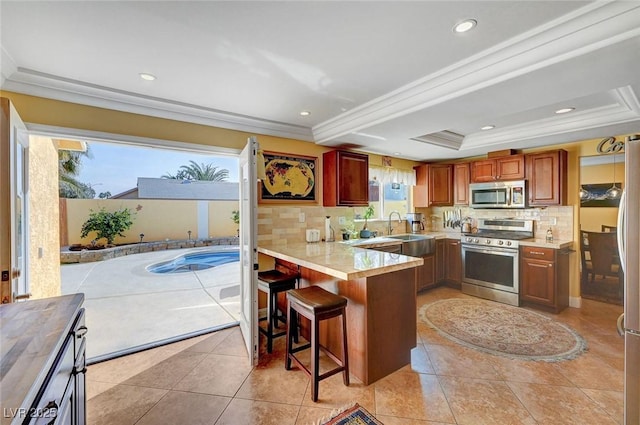 kitchen featuring sink, a kitchen breakfast bar, stainless steel appliances, a tray ceiling, and kitchen peninsula